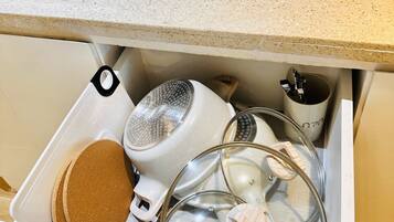 A kitchen drawer with a white countertop above, containing a white kettle, a glass container, and a wooden spoon.