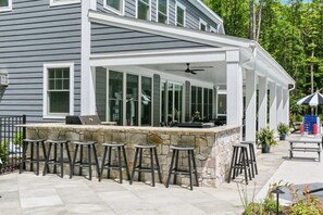 A covered outdoor area with a stone countertop, bar stools, and a ceiling fan.