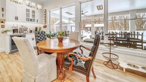 A dining area with a round wooden table, two upholstered chairs, and a tall, narrow side table with a glass top. - Pier Cove Estate - Pool, Pickleball, Hot Tub, Firepit - Sleeps up to 23 (Fennville)