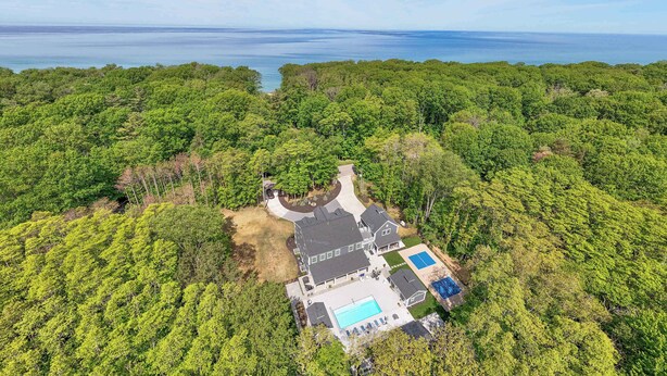An aerial view of a property with a swimming pool, a tennis court, and a large house surrounded by dense forest. - Pier Cove Estate - Pool, Pickleball, Hot Tub, Firepit - Sleeps up to 23 (Fennville)