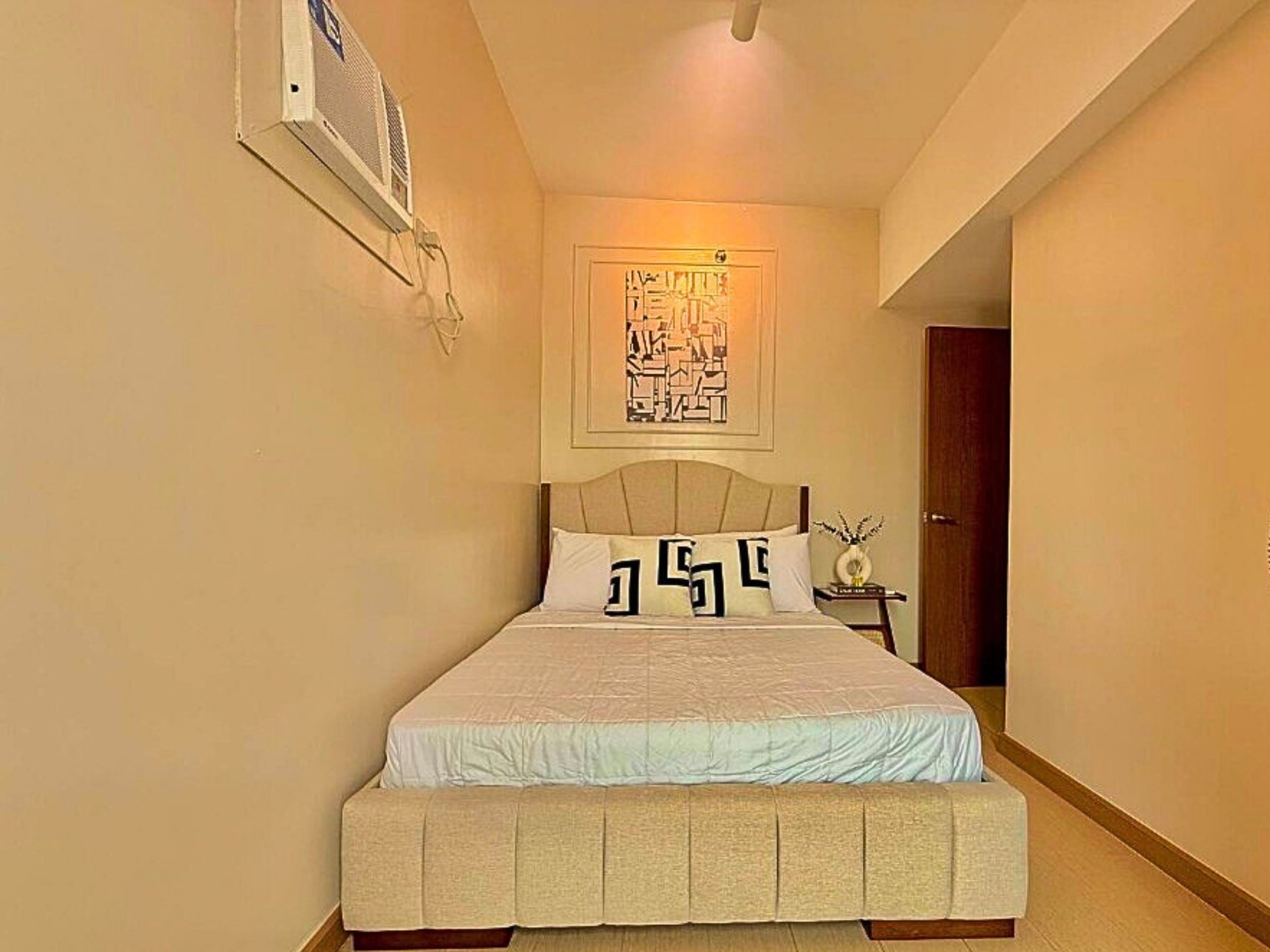 A bedroom with a bed, a nightstand, a wall-mounted air conditioner, and a door.