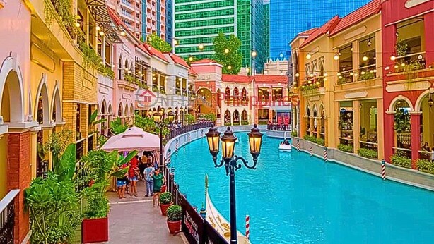 A canal with buildings on either side, a boat in the water, and people walking along the path.