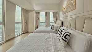 A modern hotel room with large windows, a bed with a quilted cover, and a headboard with decorative pillows.