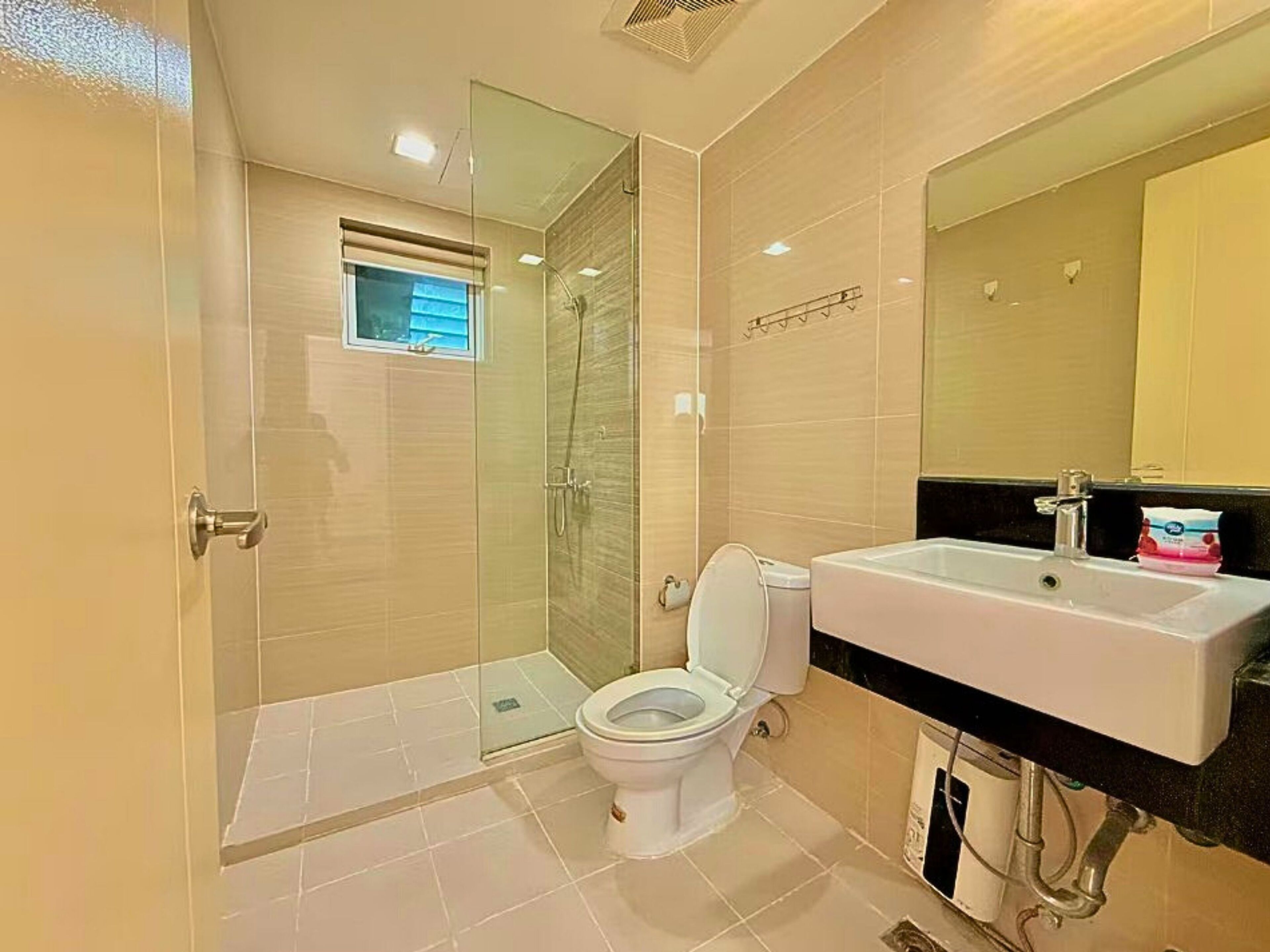 Un baño moderno con ducha separada por mampara de vidrio, inodoro blanco y lavamanos con espejo.