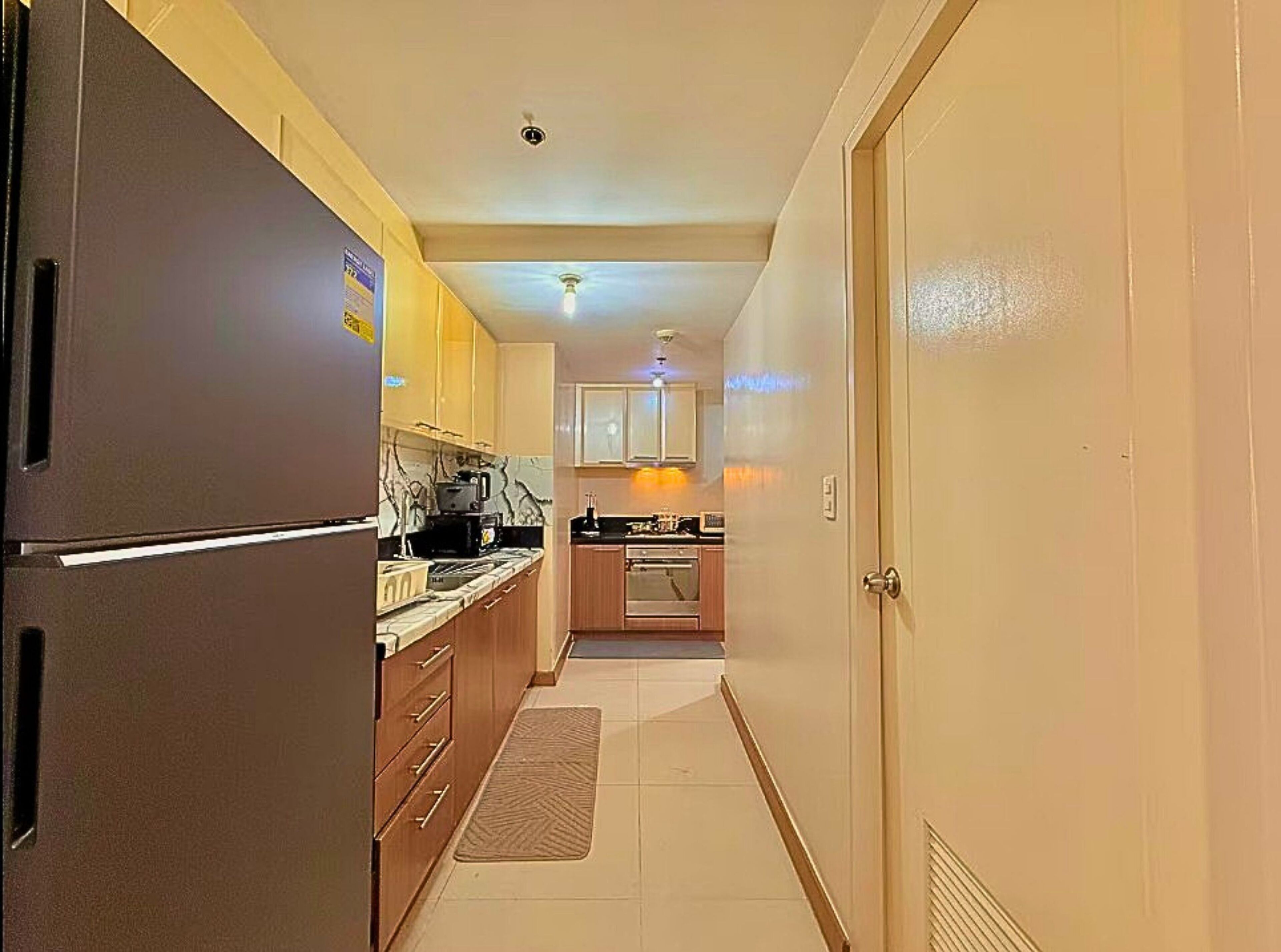 A narrow hallway leading to a kitchen with a refrigerator, cabinets, and a microwave.