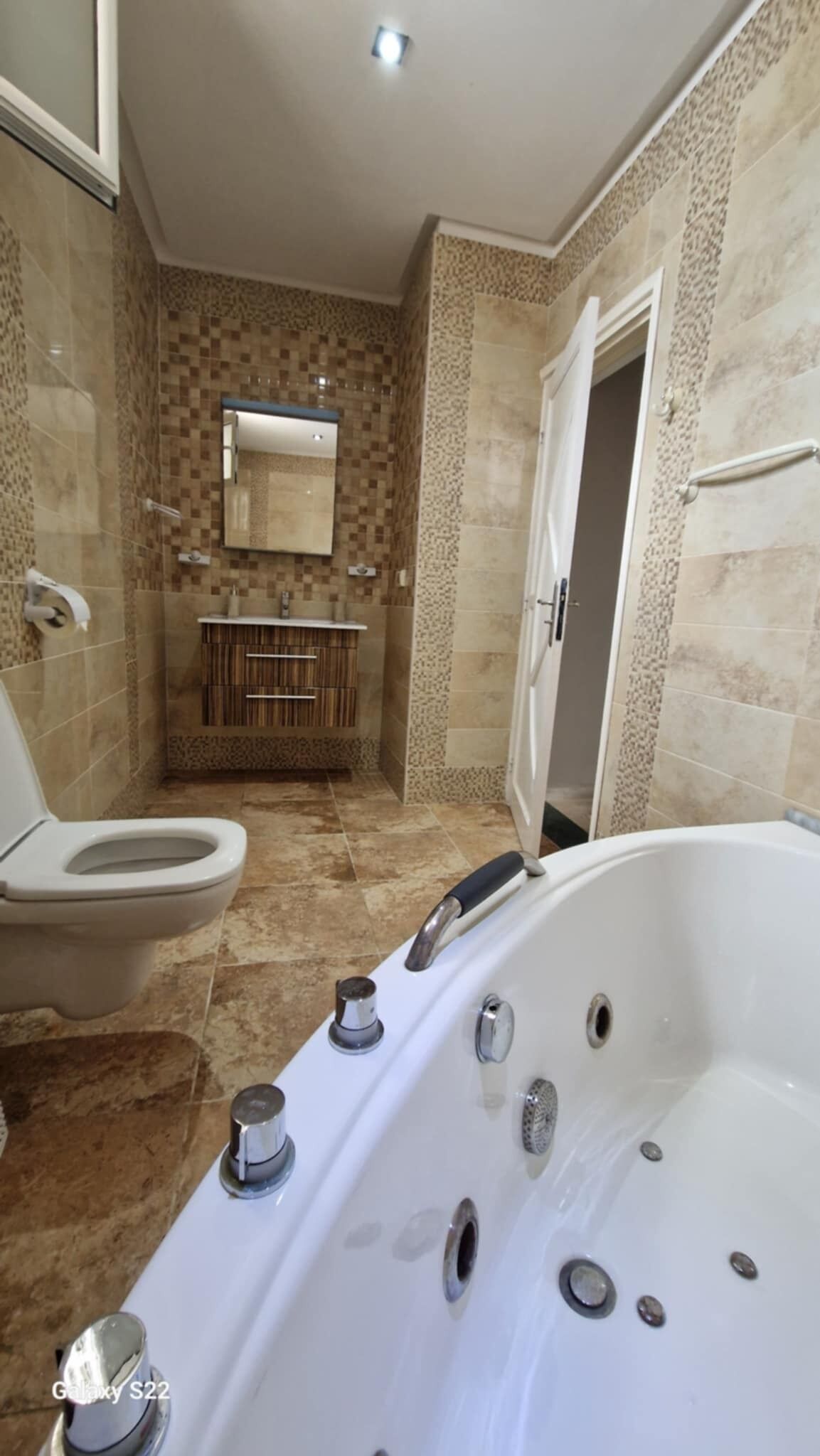 A bathroom with a toilet, sink, mirror, and a large bathtub.