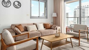 Una sala de estar moderna con un sofá color beige, sillas de madera, una mesa de centro de madera y dos obras de arte en la pared.