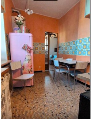 Eine kleine Küche mit Kühlschrank, zwei Stühlen, einem Esstisch und einer gefliesten Spritzschutzwand.