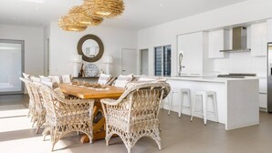 Una cocina moderna con una isla central, armarios blancos y un comedor con sillas de mimbre y una mesa de madera.