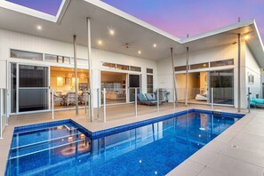 Une maison moderne dotée d’une piscine, de grandes portes vitrées et d’un espace patio.