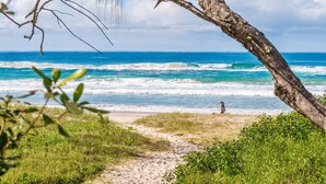 Una playa con una vista despejada del océano, un sendero arenoso que lleva al agua y una persona caminando por la orilla.