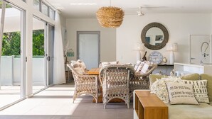 Un espacio habitable amplio y luminoso con mobiliario de mimbre, un espejo grande y una zona de comedor.