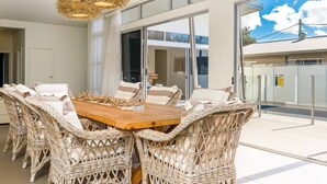 Un comedor con mobiliario de mimbre y una mesa de madera, ventanas amplias y vistas al exterior.
