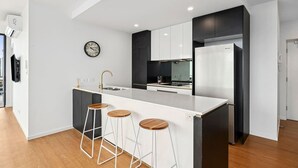 A modern kitchen with a central island, bar stools, a clock, and a refrigerator. - Skyline Serenity - Modern Escape + Stunning Views (Surfers Paradise)