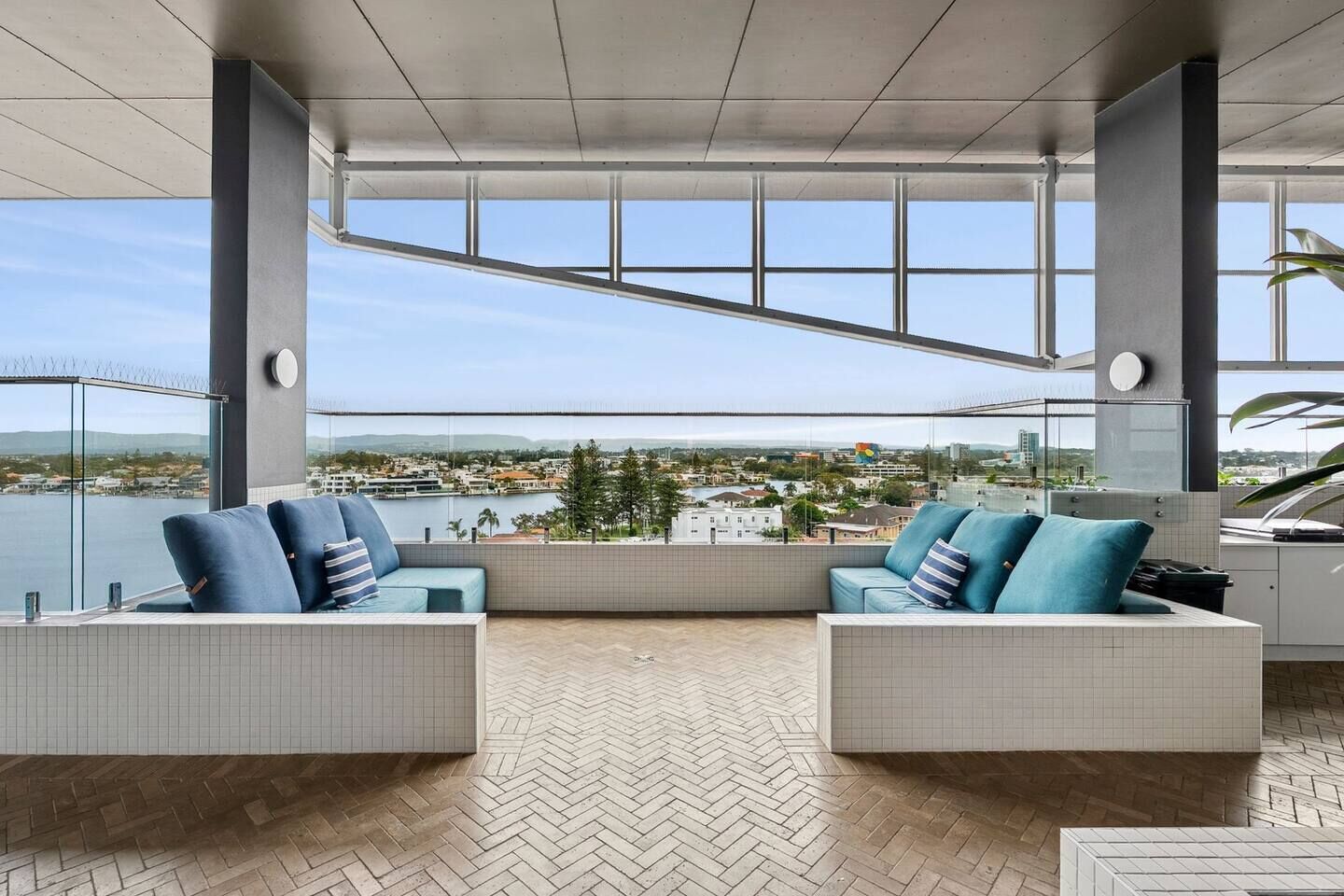 Ein moderner Außenbereich mit zwei Sofas und einem Fischgrätparkettboden, mit Blick auf eine Stadtlandschaft und Wasser.