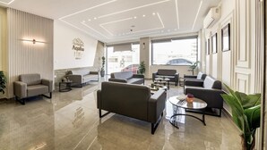 En modern hotellobby med en stilren och minimalistisk design, med en sittgrupp bestående av soffor och ett soffbord, en receptionsdisk och ett stort fönster med utsikt över gatan.