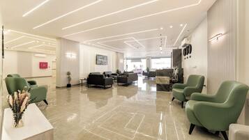 A modern lobby with a polished floor, green armchairs, a reception desk, and a large painting on the wall.
