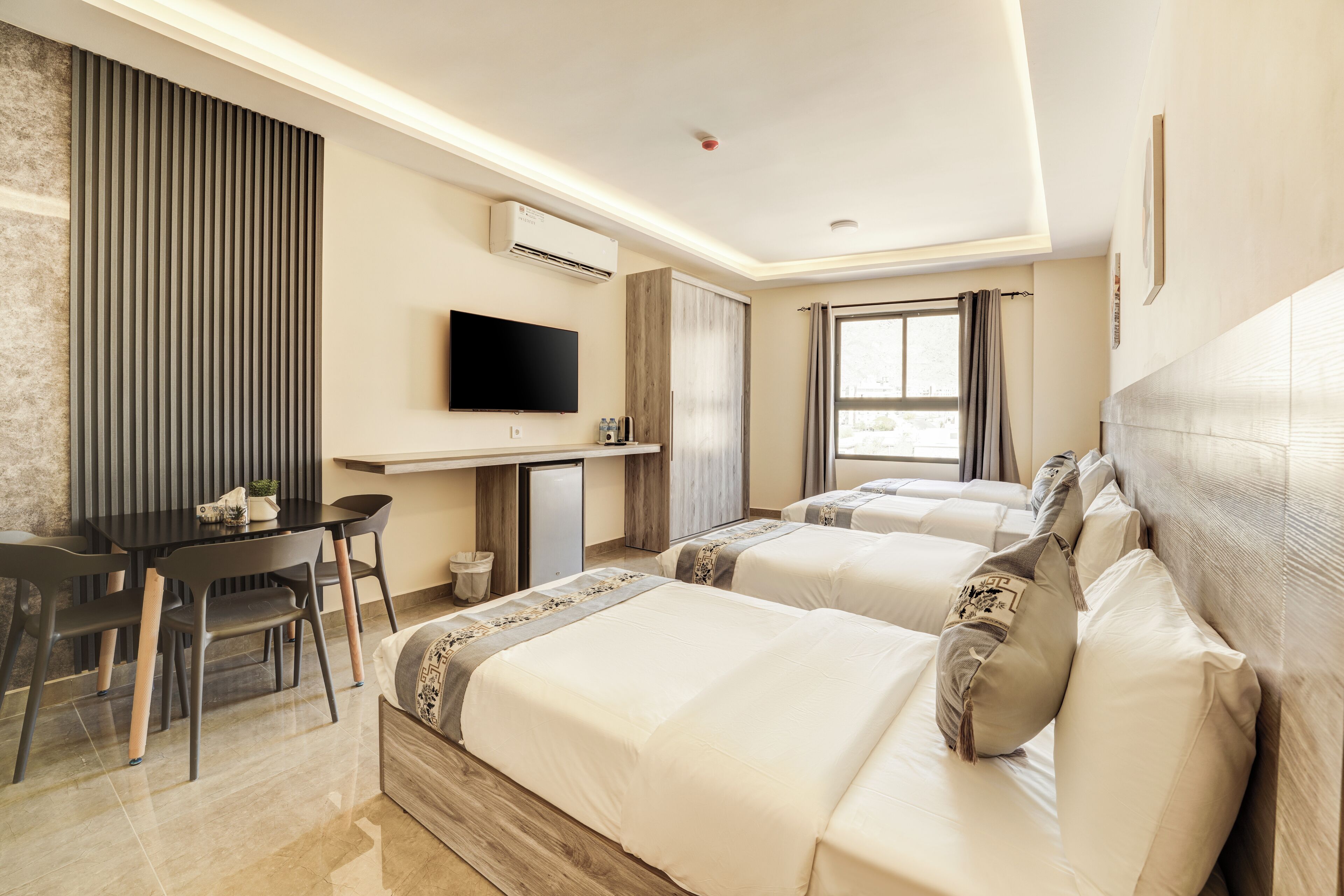 A hotel room with two beds, a desk, a TV, and a window with curtains.