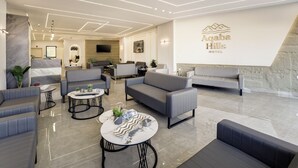 En modern hotellobby med grå soffor, ett marmorbord och en stor vägg med hotellets namn.