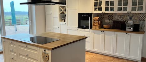 A modern kitchen with white cabinetry, a central island with a built-in induction cooktop, and a view of the outdoors through a large window.
