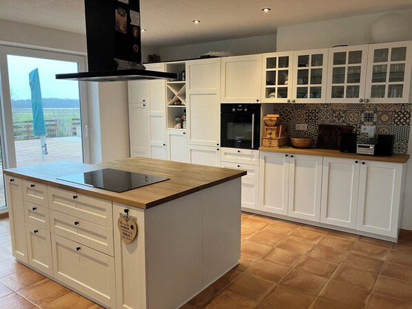 Una cocina moderna con armarios blancos, una isla central con placa de inducción integrada y vistas al exterior a través de un ventanal.