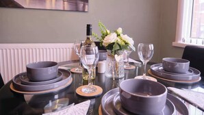 A dining table set with grey bowls, wine glasses, and a bottle of white wine. - 3BR Modern House, Garden, Parking, Sleeps 6, Wifi (Strabane)