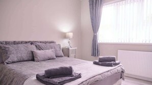 A bedroom with a bed, a nightstand, a lamp, and a window with curtains. - 3BR Modern House, Garden, Parking, Sleeps 6, Wifi (Strabane)