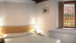 A bedroom with a wooden headboard, two bedside lamps, a bed with white bedding, a small picture on the wall, and a window with a view of a wooden fence. - Apartment 5 (Castel del Piano)