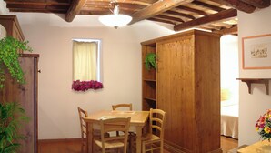A wooden dining table with four chairs, a window with a curtain, and a wooden cabinet with shelves. - Apartment 5 (Castel del Piano)