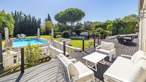Une terrasse en bois avec des meubles d’extérieur, une piscine et un grand arbre.