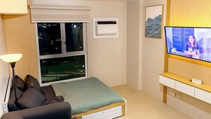 A modern bedroom with a bed, a sofa, a TV, and a window. - Cozy Condo @ Paranaque near NAIA (Paranaque City)