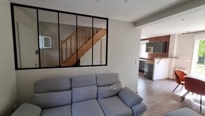 Una sala de estar moderna con un sofá gris, una escalera de madera y una zona de cocina con salpicadero de ladrillo y un microondas.