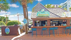 A beachside restaurant with a sign reading "Marco Polo Paradise Grill," featuring outdoor seating and a brick facade.
