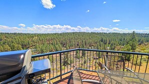 A balcony with a grill, overlooking a forested landscape.