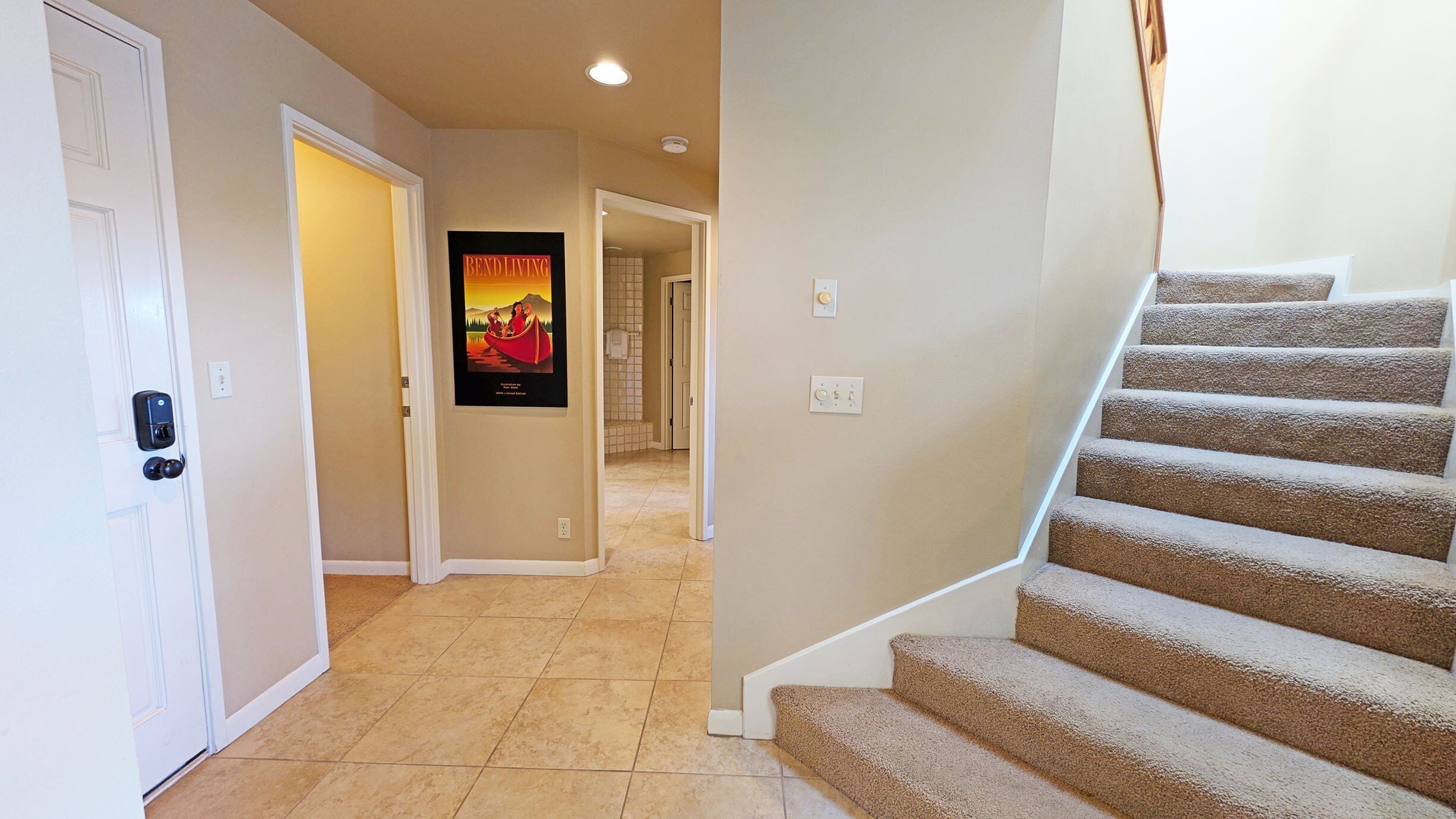 A hallway with a carpeted staircase, a door with a keypad lock, and a poster on the wall.