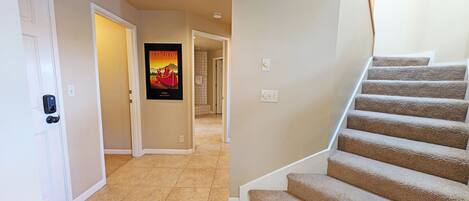 A hallway with a carpeted staircase, a door with a keypad lock, and a poster on the wall.