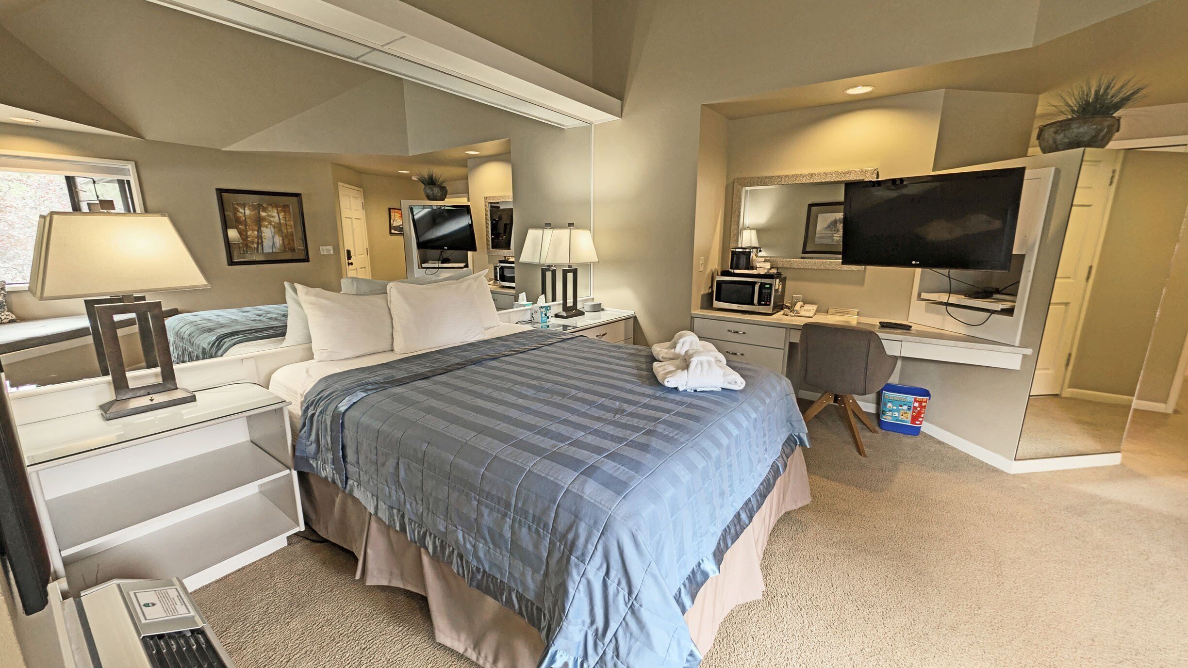 A hotel room with a bed, desk, television, and a small kitchenette.