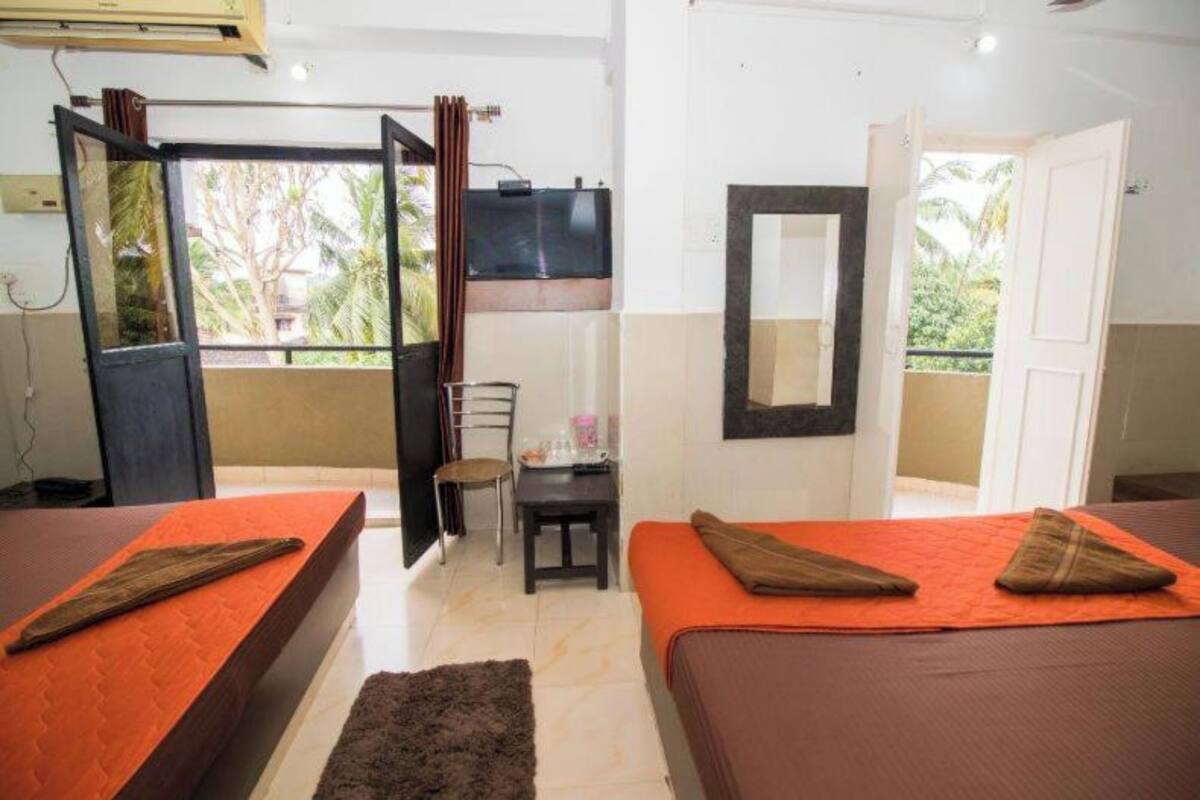 Habitación de hotel con dos camas, una mesita, una silla, un televisor y un balcón con vista a palmeras.
