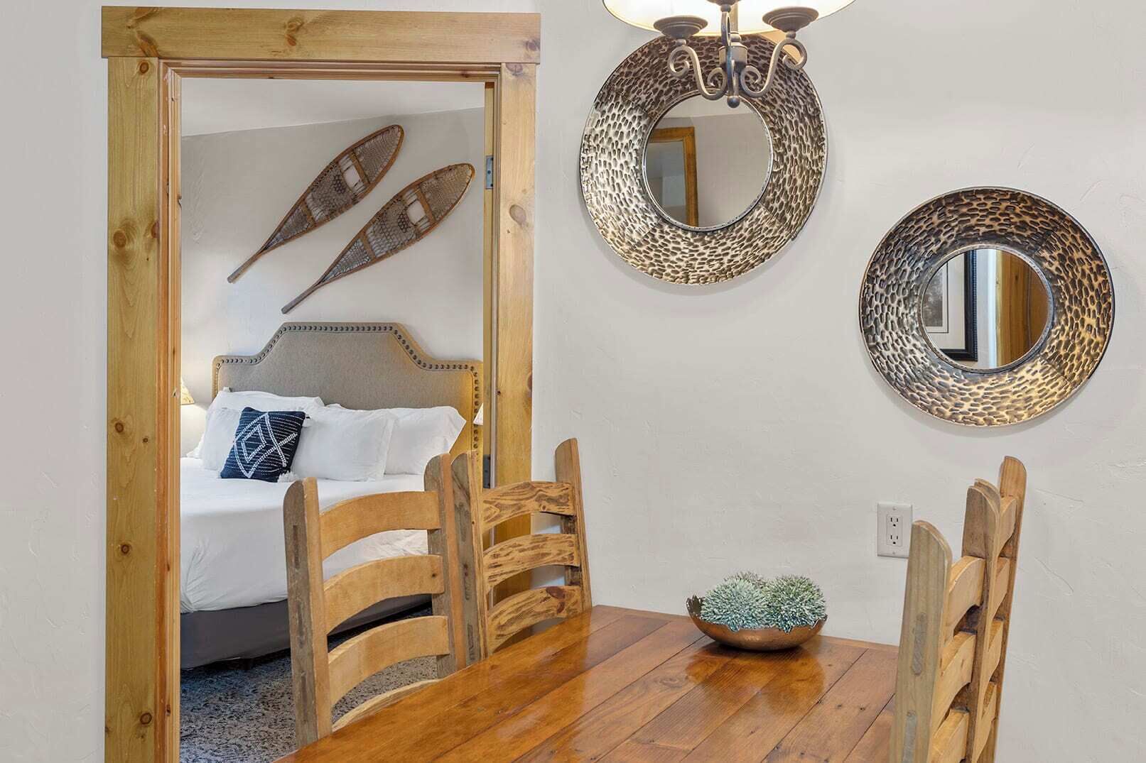 A room with a wooden bed, a dining table with chairs, and two wall-mounted mirrors.