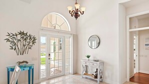 Ein geräumiger Eingangsbereich mit einer großen Glasdoor, einem weißen Konsolentisch, einem Spiegel und einer Chandelier.