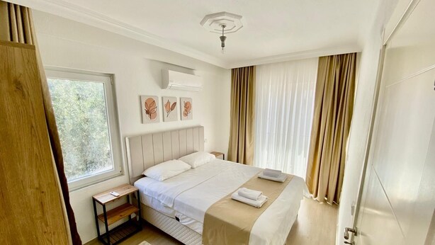 A bedroom with a large bed, a bedside table, a window with curtains, and a ceiling light. - Mitra apart (Antalya)
