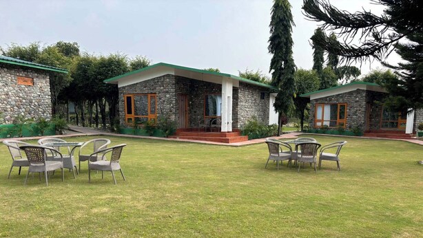 A stone building with a green roof, surrounded by a grassy lawn and several wicker chairs. - Corbett Wildernest Resort (Kotabagh)