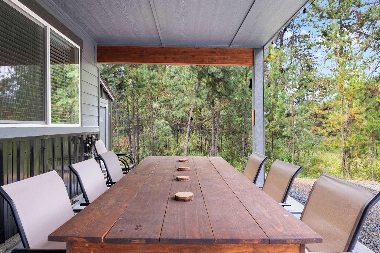 A covered outdoor dining area with a wooden table and chairs, surrounded by trees.