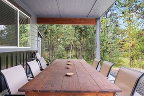 Un área de comedor al aire libre techada, con una mesa y sillas de madera, rodeada de árboles.