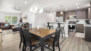 A spacious kitchen with modern appliances, a dining area with a wooden table and chairs, and a living room with a sofa and a large window.