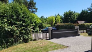 Ein von einer Mauer gesäumter Weg führt zu einem Haus mit gepflasterter Auffahrt, auf der ein Auto geparkt ist.