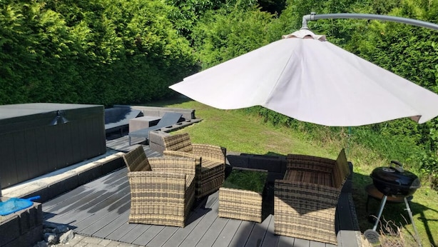 Eine Terrasse im Freien mit Korbmöbeln, einem Grill und einem großen Sonnenschirm.