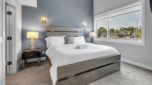 A bedroom with a large bed, two bedside lamps, a nightstand, and a window with a view of the outside. - Opulent Birmingham Retreat (Birmingham)