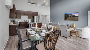 A modern kitchen with dark wooden cabinets, a stainless steel refrigerator, and a dining area with a glass table and wooden chairs. - Opulent Birmingham Retreat (Birmingham)