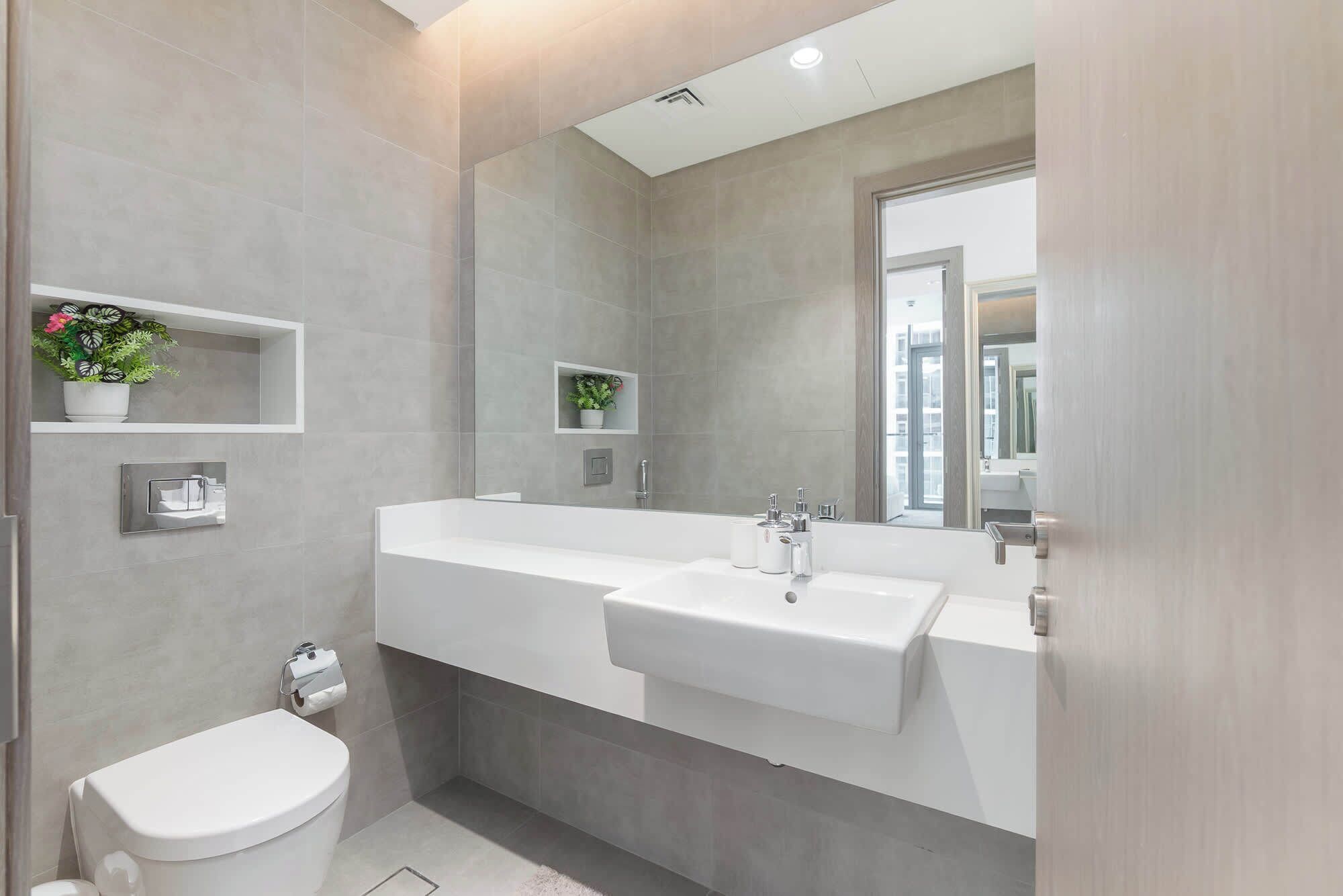 Een moderne badkamer met een grote spiegel, twee wasbakken, een toilet en een douchehoek.
